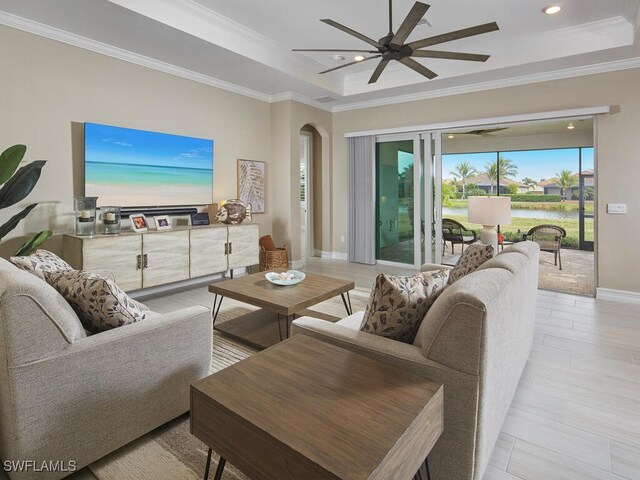 living room with ceiling fan, ornamental molding, a water view, and a raised ceiling