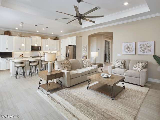 living room featuring ceiling fan, sink, a tray ceiling, and ornamental molding