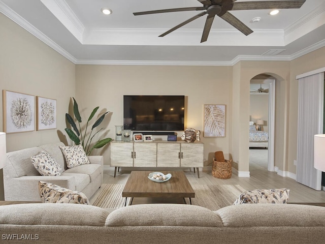 living room featuring crown molding, ceiling fan, a tray ceiling, and light hardwood / wood-style floors