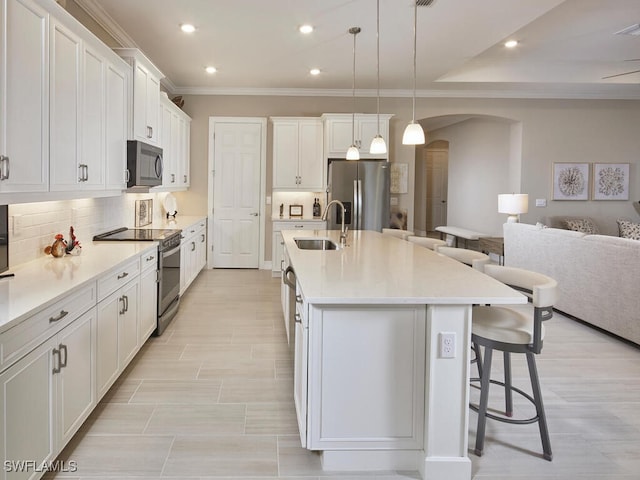 kitchen with pendant lighting, sink, white cabinets, stainless steel appliances, and a center island with sink