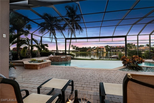 pool at dusk featuring a lanai, a water view, a patio area, and an in ground hot tub