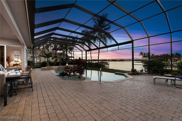 pool at dusk with a lanai, a water view, and a patio area