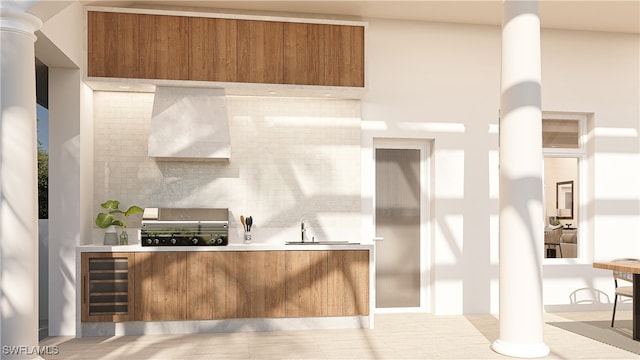 kitchen featuring decorative backsplash, sink, wall chimney exhaust hood, beverage cooler, and ornate columns