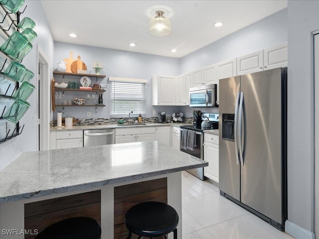 kitchen with white cabinetry, stainless steel appliances, a kitchen breakfast bar, light stone counters, and sink