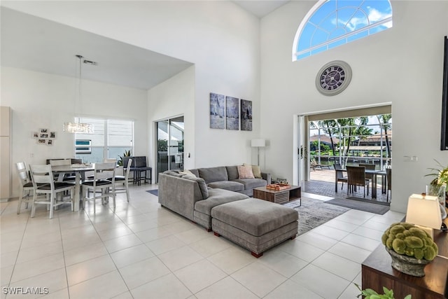 living room featuring a water view, a towering ceiling, light tile patterned floors, and a notable chandelier