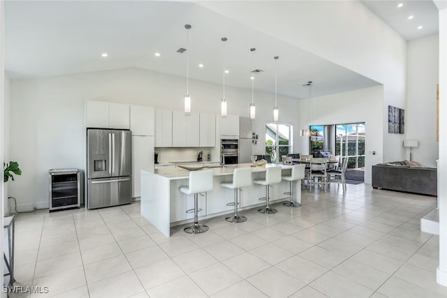 kitchen with appliances with stainless steel finishes, a kitchen island with sink, high vaulted ceiling, white cabinets, and decorative light fixtures