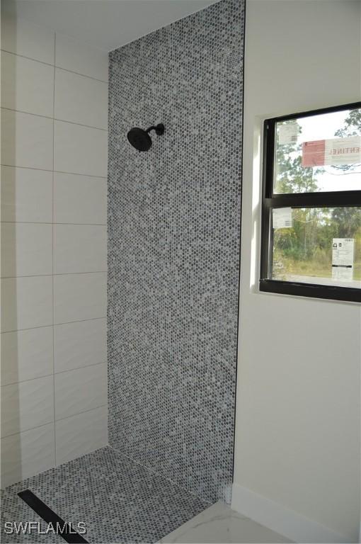 bathroom with marble finish floor and a tile shower