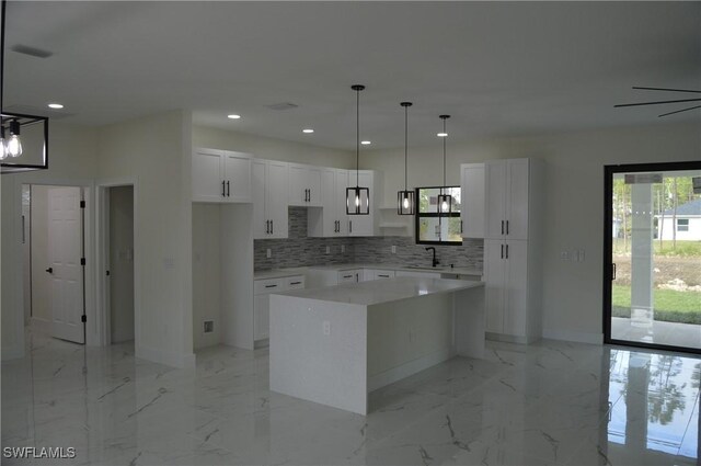 kitchen featuring sink, a kitchen island, pendant lighting, decorative backsplash, and white cabinets