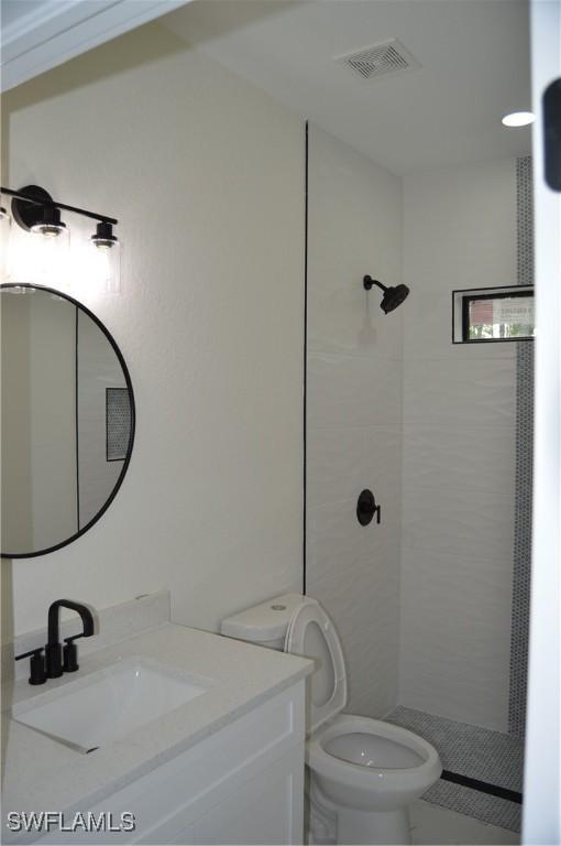 bathroom with tiled shower, vanity, and toilet