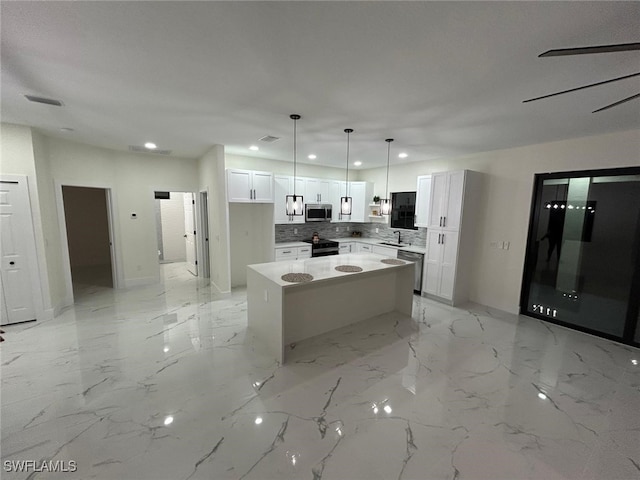 kitchen featuring tasteful backsplash, stainless steel microwave, white cabinetry, a kitchen island, and a sink