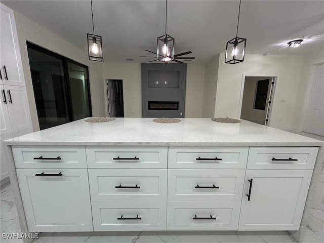 kitchen with light stone countertops, white cabinetry, marble finish floor, a center island, and decorative light fixtures