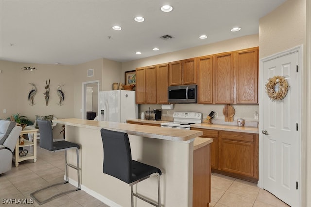 kitchen featuring white appliances, a kitchen bar, a kitchen island, and light tile patterned floors