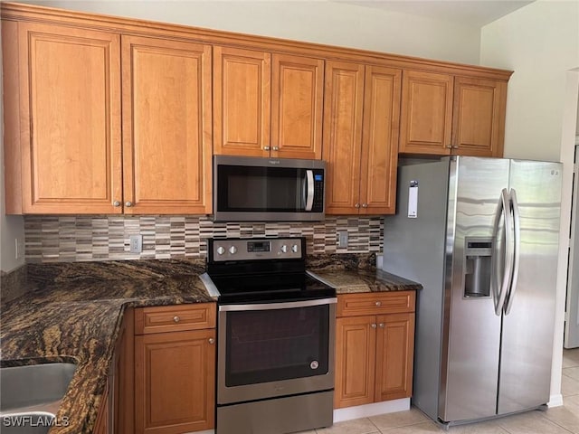 kitchen featuring sink, light tile patterned floors, appliances with stainless steel finishes, decorative backsplash, and dark stone counters