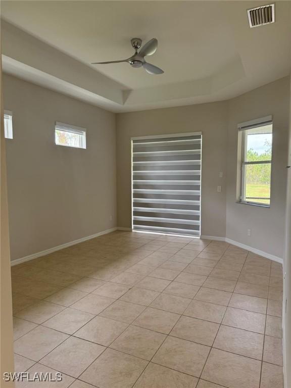 empty room featuring ceiling fan, a raised ceiling, and light tile patterned floors