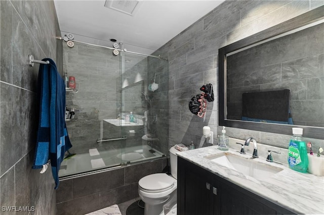 full bathroom with enclosed tub / shower combo, tile walls, vanity, and toilet