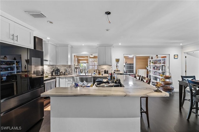 kitchen featuring stainless steel fridge, a breakfast bar area, white cabinetry, backsplash, and ornamental molding