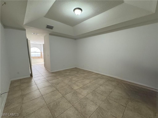 empty room featuring a textured ceiling, light tile patterned flooring, and a tray ceiling