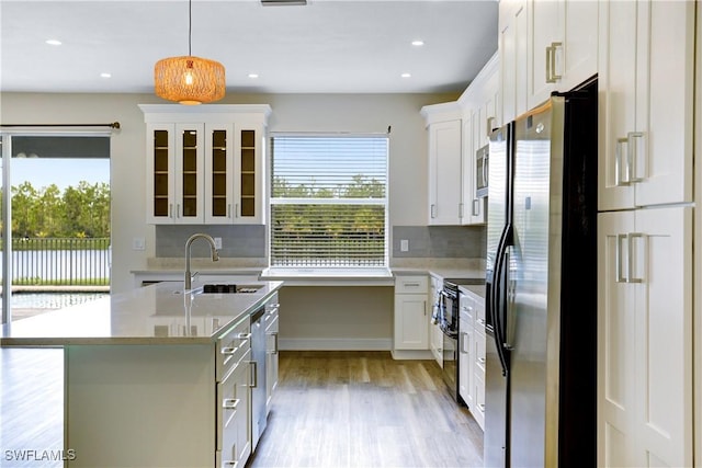 kitchen featuring appliances with stainless steel finishes, backsplash, a kitchen island with sink, decorative light fixtures, and white cabinets