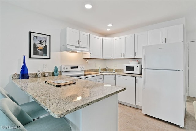 kitchen with a breakfast bar, white cabinets, light stone counters, kitchen peninsula, and white appliances