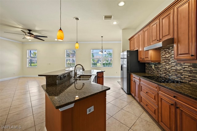 kitchen featuring black stovetop, sink, dark stone counters, hanging light fixtures, and a kitchen island with sink