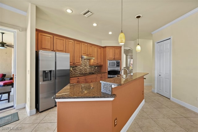 kitchen with pendant lighting, appliances with stainless steel finishes, backsplash, an island with sink, and dark stone counters