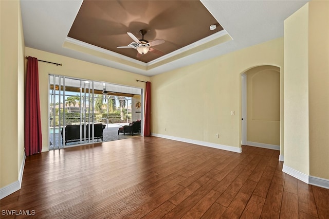 empty room with a raised ceiling, crown molding, hardwood / wood-style flooring, and ceiling fan