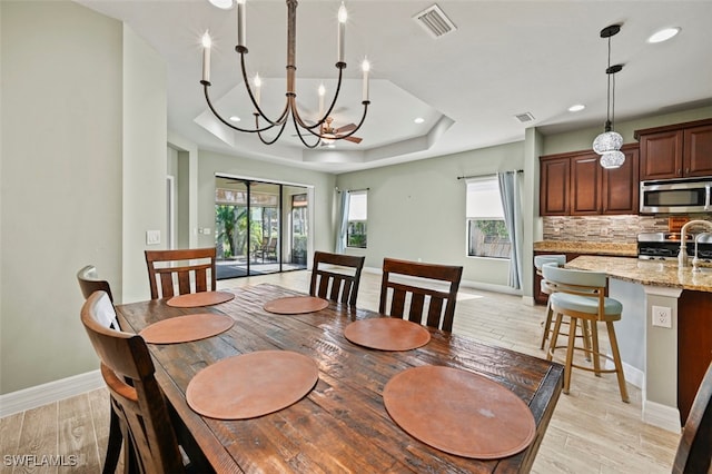 dining space featuring a tray ceiling, sink, and light wood-type flooring