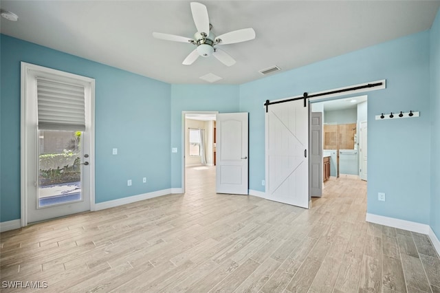 unfurnished bedroom with multiple windows, a barn door, access to exterior, and light hardwood / wood-style flooring