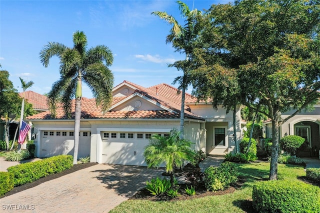 mediterranean / spanish-style house featuring a tile roof, decorative driveway, an attached garage, and stucco siding