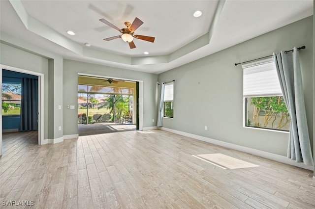 empty room with ceiling fan, a tray ceiling, and light wood-type flooring