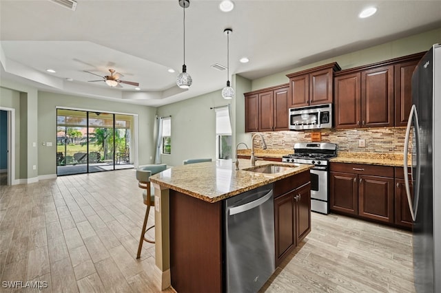 kitchen with appliances with stainless steel finishes, sink, hanging light fixtures, a raised ceiling, and a center island with sink