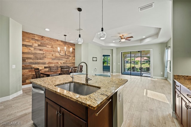 kitchen featuring sink, a center island with sink, a tray ceiling, dishwasher, and light stone countertops