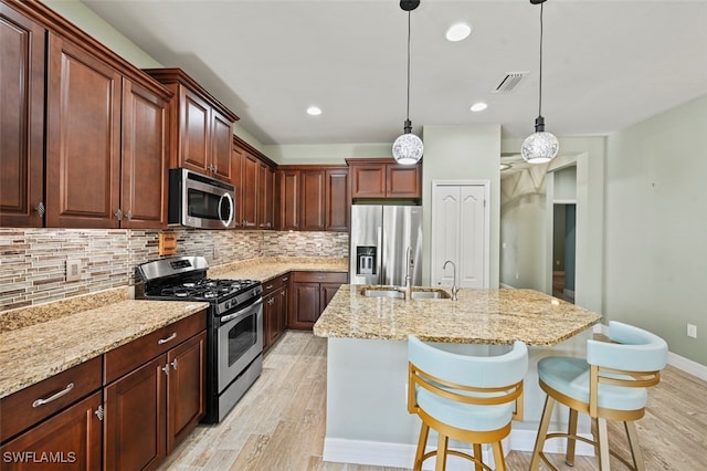 kitchen with a breakfast bar, tasteful backsplash, light hardwood / wood-style flooring, appliances with stainless steel finishes, and an island with sink