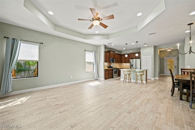 living room with a tray ceiling, ceiling fan with notable chandelier, and light wood-type flooring