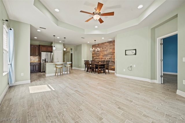 unfurnished living room with a raised ceiling, ceiling fan with notable chandelier, and light hardwood / wood-style floors