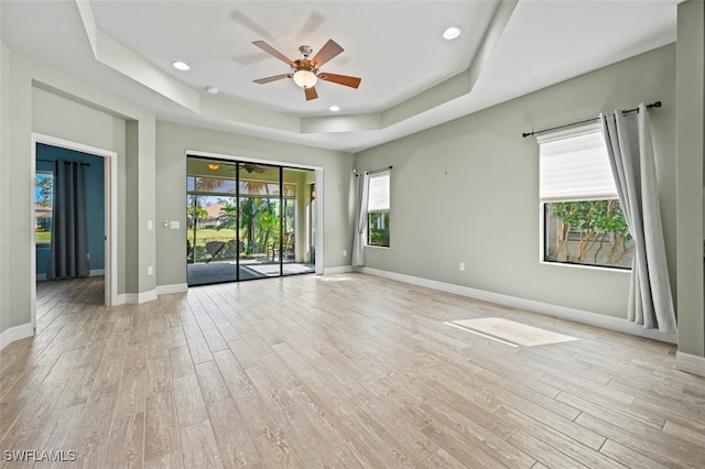 empty room featuring ceiling fan, a tray ceiling, and light hardwood / wood-style flooring