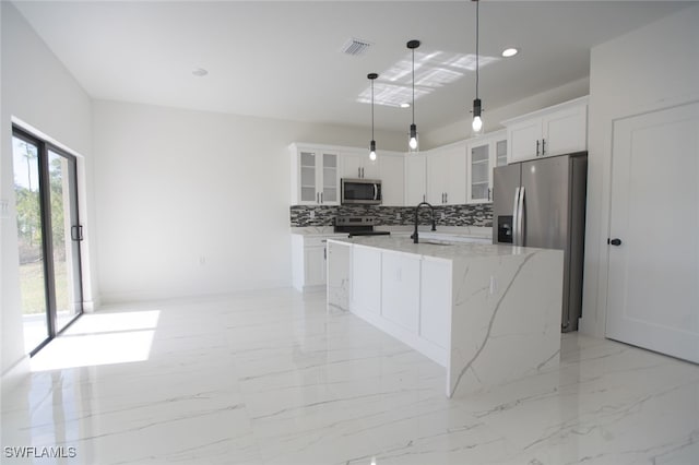 kitchen featuring hanging light fixtures, appliances with stainless steel finishes, an island with sink, white cabinets, and backsplash