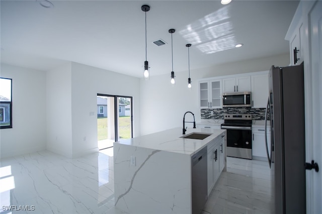 kitchen with an island with sink, sink, white cabinets, hanging light fixtures, and stainless steel appliances