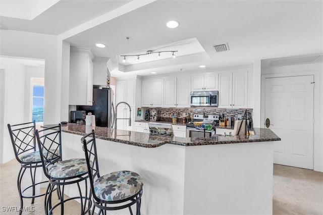 kitchen with white cabinets, appliances with stainless steel finishes, dark stone countertops, kitchen peninsula, and a breakfast bar