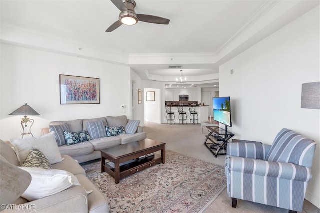 living room with light colored carpet, ornamental molding, ceiling fan with notable chandelier, and a raised ceiling