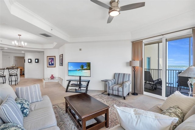 living room featuring ceiling fan with notable chandelier, a tray ceiling, ornamental molding, and light carpet