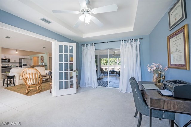 carpeted office space featuring a raised ceiling, ceiling fan, and french doors