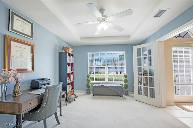 carpeted office with ceiling fan and a tray ceiling