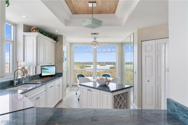 kitchen featuring sink, white cabinetry, light tile patterned floors, a tray ceiling, and ornamental molding