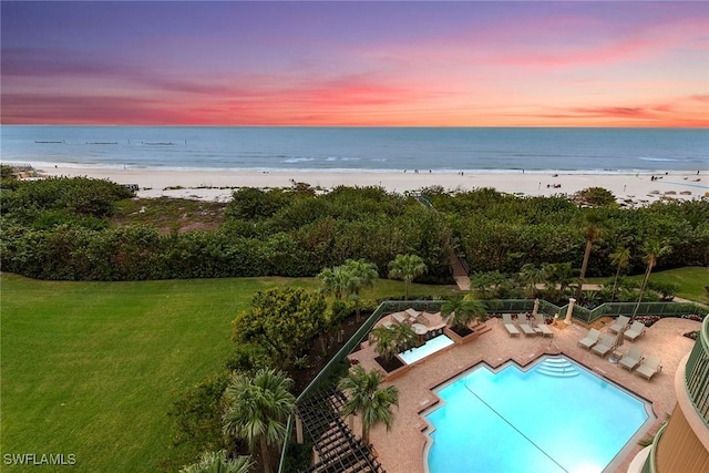 pool at dusk featuring a lawn, a water view, and a beach view