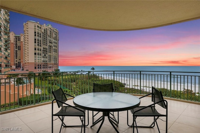 balcony at dusk with a water view and a view of the beach