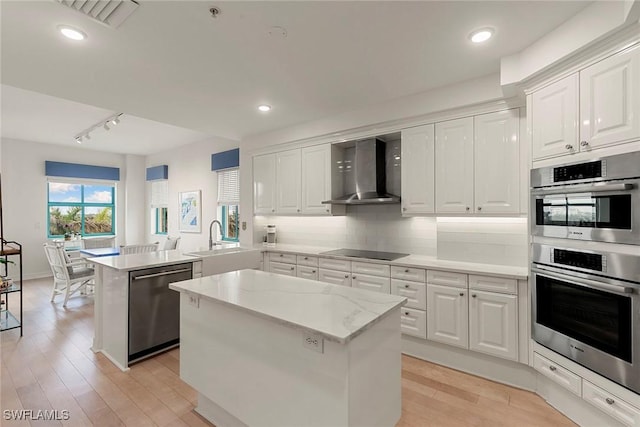 kitchen with kitchen peninsula, appliances with stainless steel finishes, wall chimney exhaust hood, white cabinets, and a center island