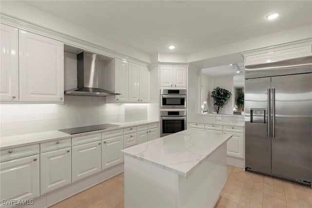 kitchen with white cabinets, wall chimney exhaust hood, a kitchen island, stainless steel appliances, and decorative backsplash