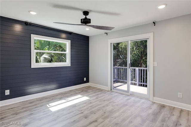 spare room featuring ceiling fan, wooden walls, and light hardwood / wood-style flooring