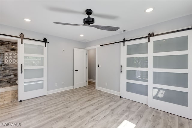 unfurnished bedroom featuring ceiling fan, connected bathroom, a barn door, and light hardwood / wood-style floors